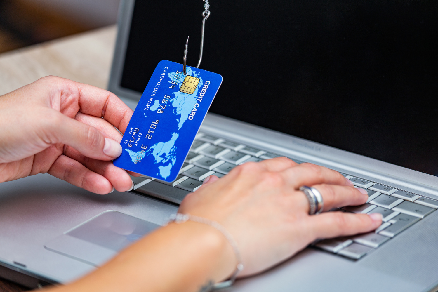 phishing ręka z kartą kredytową na haczyku przy komputerze